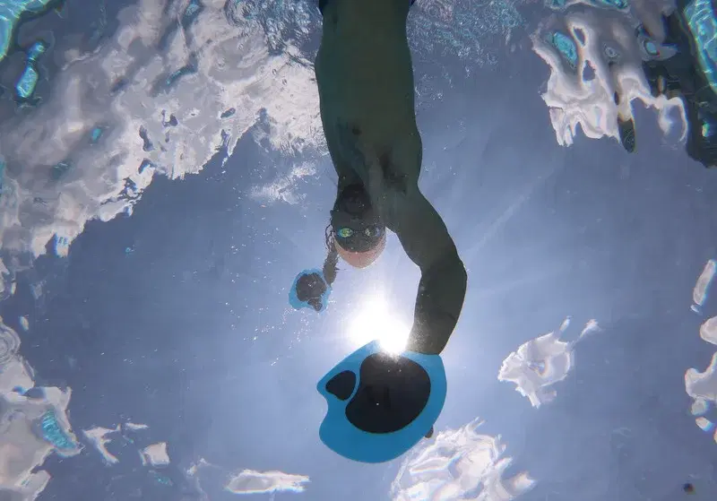A swimmer practicing underwater with training paddles